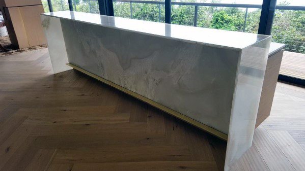 Minimalist bar with a brass foot rail and a sleek marble-like finish on herringbone wood flooring.