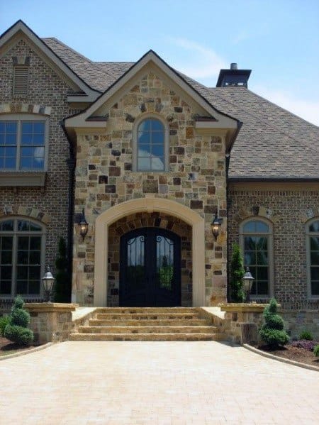 Grand home with mixed stone and brick exterior, arched wrought iron entry doors, elegant steps, and symmetrical landscaping