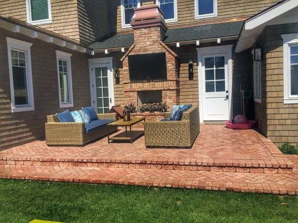 Brick patio with wicker furniture, a cozy fireplace, and mounted TV