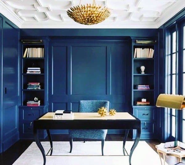 Stunning home office with bold navy blue built-in bookcases, modern desk, and a gold statement chandelier