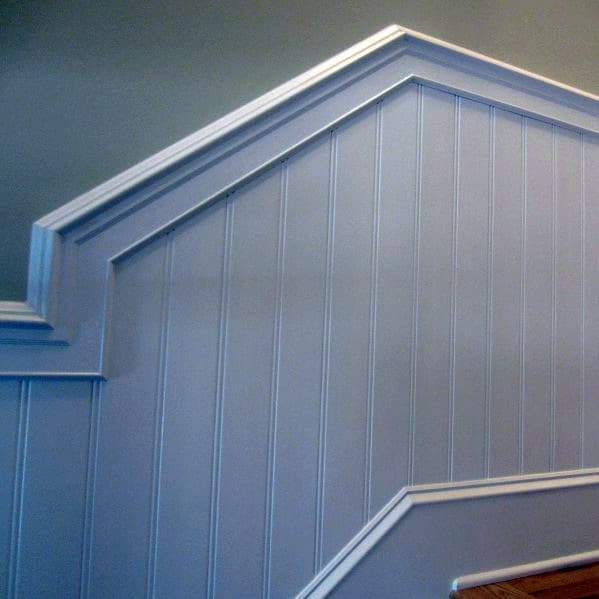 A staircase with white wood paneling, chair rail detailing, and a wooden handrail against a light gray wall
