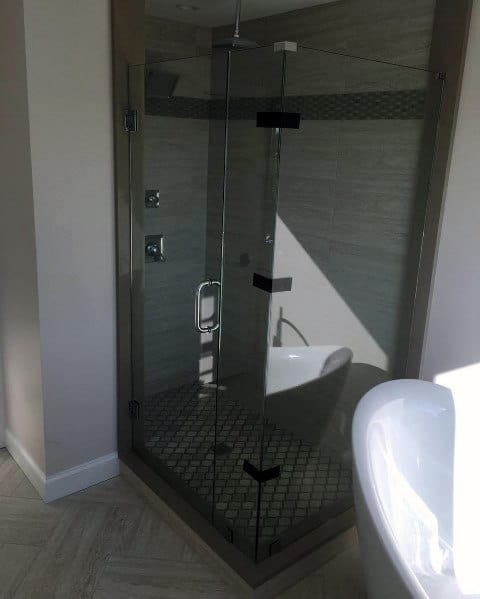 Corner glass shower enclosure in a modern bathroom with gray tiles and a partial view of a white bathtub