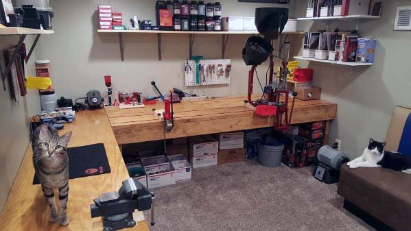 Spacious reloading bench with mounted presses, organized storage shelves, and a cozy setting complete with two curious cats