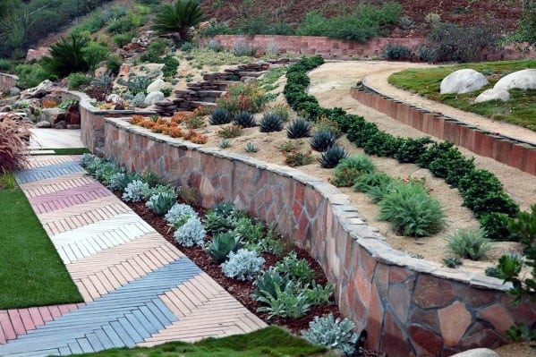 Stunning sloped landscape with tiered stone retaining walls, drought-tolerant plants, and a colorful geometric paved walkway