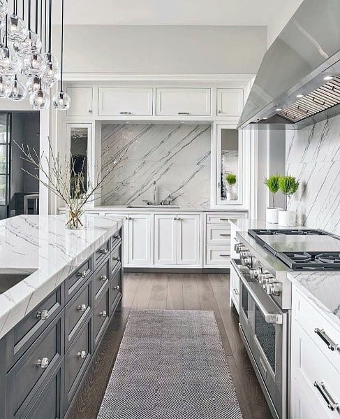 Elegant kitchen with white marble backsplash, two-tone cabinetry, stainless steel appliances, and a statement chandelier