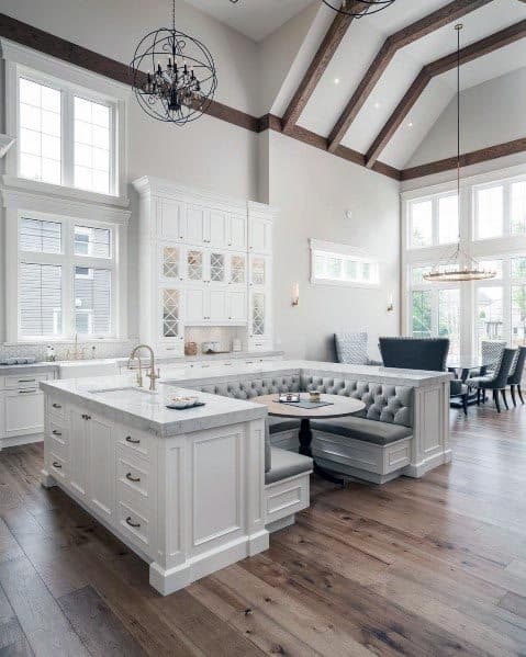 White kitchen with marble island, built-in dining nook, high ceilings, and exposed beams.