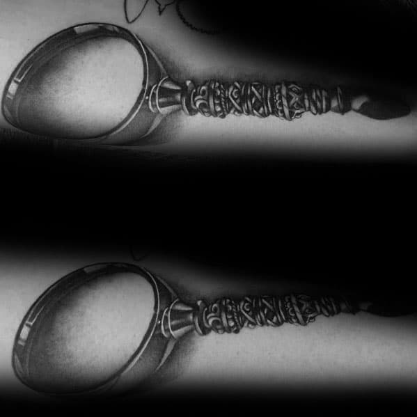 Tattoo of a magnifying glass with a highly detailed, ornate handle, featuring realistic shading and depth for a bold and vintage-inspired design.
