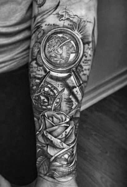 Tattoo featuring a magnifying glass over a world map, a compass, and roses, designed with deep shading for a bold and intricate travel-themed look.