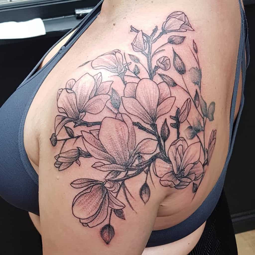 Black and gray floral tattoo beautifully adorns the shoulder and upper arm, showcasing blooming flowers and buds