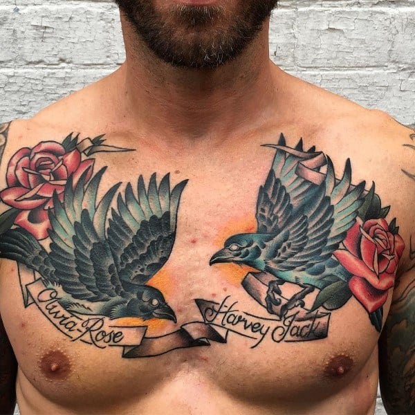 Traditional-style chest tattoo featuring two magpies in flight, red roses, banners with names, and an orange background for a bold, symbolic design.