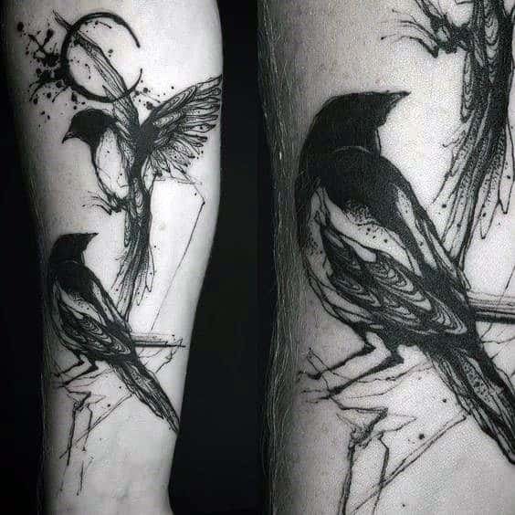 Abstract black ink magpie tattoo on forearm, featuring one bird perched and another in flight with artistic splatter and sketch-like details.