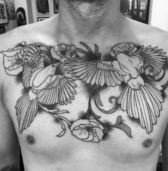 Black and gray chest tattoo featuring two magpies in flight among detailed flowers and vines, creating an elegant and nature-inspired design.