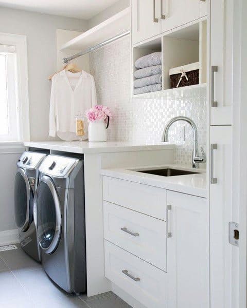 Bright laundry room with white cabinets, mosaic backsplash, and modern silver appliances.
