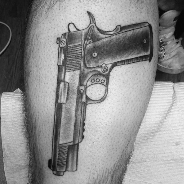 Black and gray tattoo of a 1911 pistol on the thigh, featuring bold outlines and shading for a detailed and realistic appearance.