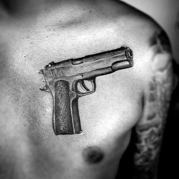 Realistic black and gray tattoo of a 1911 pistol on the upper chest, designed with fine details and shading for a bold three-dimensional effect.
