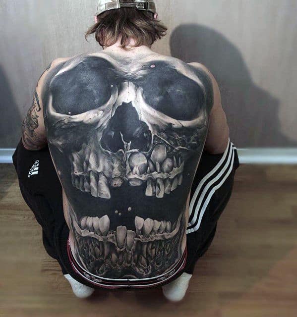 Massive hyper-realistic skull back tattoo with bold black shading and detailed teeth stretching from shoulders to lower back.
