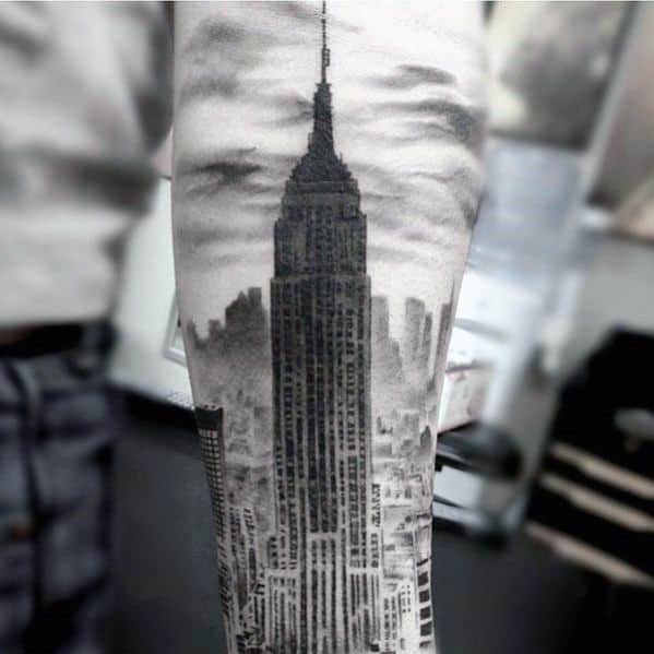 Realistic black and gray tattoo of the Empire State Building towering over the New York City skyline on the forearm.