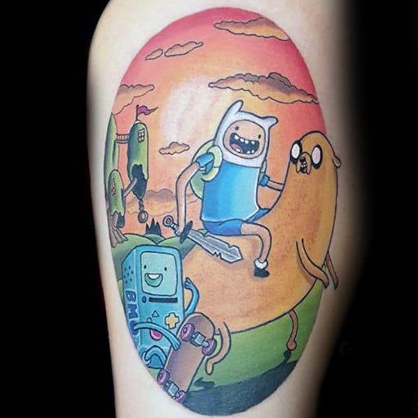 Adventure Time tattoo of Finn riding Jake with BMO in front, set against a colorful sunset landscape, inked on the upper arm.