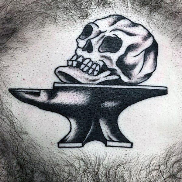 Black and grey anvil tattoo on the chest with a realistic skull resting on top, featuring bold shading and strong contrast for dramatic impact.