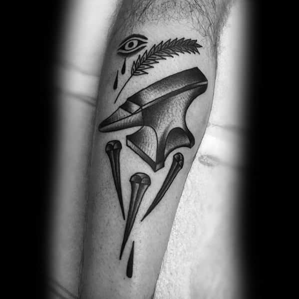 Blackwork anvil tattoo on the forearm featuring nails, a teardrop, the Eye of Providence, and a palm leaf for a symbolic, bold composition.