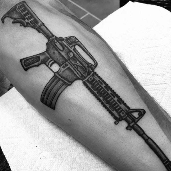 Black and grey AR-15 tattoo on the leg, featuring detailed shading and a tactical grip, symbolizing strength, precision, and firearm appreciation.