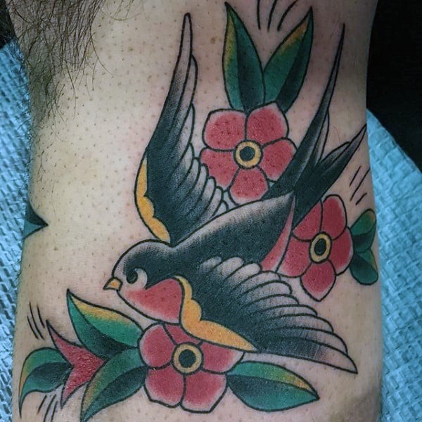 Tattoo of a sparrow in flight surrounded by red flowers with green leaves