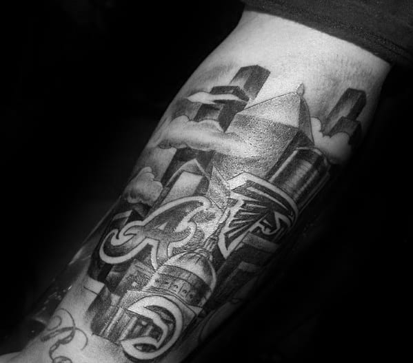 Detailed black and gray tattoo of Atlanta skyline with Falcons logo, Braves “A”, Georgia Capitol, and clouds blending into buildings.
