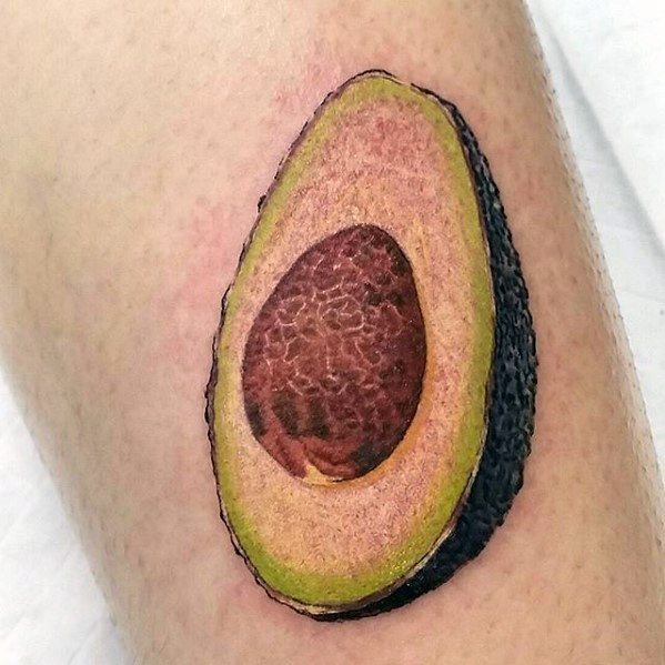 Hyper-realistic avocado tattoo with detailed textures and shading, showcasing the seed, creamy flesh, and bumpy dark skin.