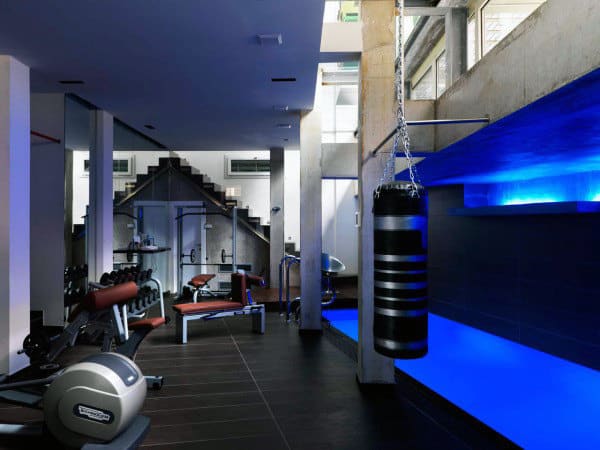Modern gym with exercise machines, weights, and a punching bag next to a blue LED-lit water feature for the home