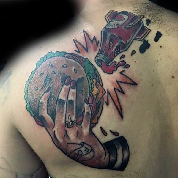 Tattoo of a hand clutching a cheeseburger with ketchup splattering on a person's shoulder