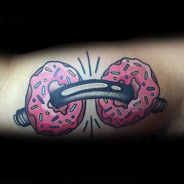 Fun and quirky tattoo of a barbell with pink sprinkled donuts as weights, symbolizing balance between fitness and indulgence.