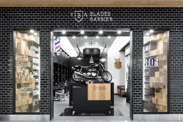 Barbershop storefront with motorcycle display, black brick facade, and modern interior lighting.