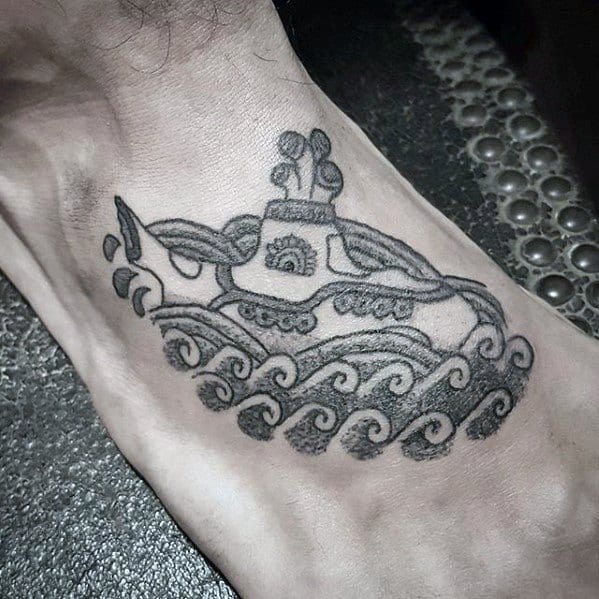 Black ink foot tattoo of The Beatles' Yellow Submarine riding stylized ocean waves, drawn with bold outlines and playful detailing.