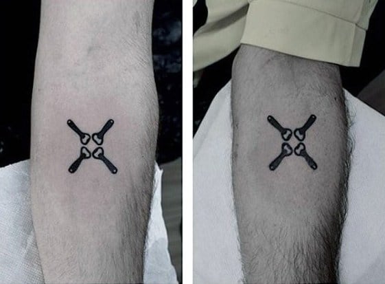 Minimalist black ink tattoo of a symmetrical four-wrench design arranged in an X shape, placed on the inner forearm for a clean, mechanical look.