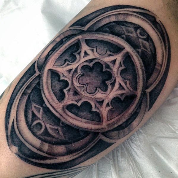 Black and grey geometric tattoo with a 3D effect, featuring intricate circular patterns and gothic-style details on the inner bicep