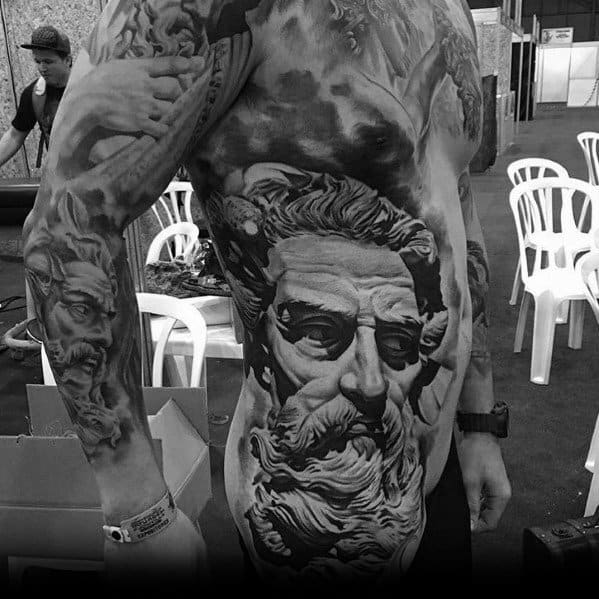 Black and grey full-torso and sleeve tattoo featuring a highly detailed, realistic Greek god-like figure with flowing beard, intense shading, and dramatic depth.