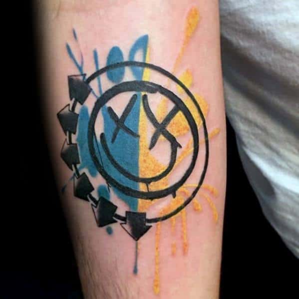 Tattoo of the Blink-182 smiley face logo with bold black outlines, featuring blue and yellow watercolor splashes behind it, creating a vibrant and dynamic design.