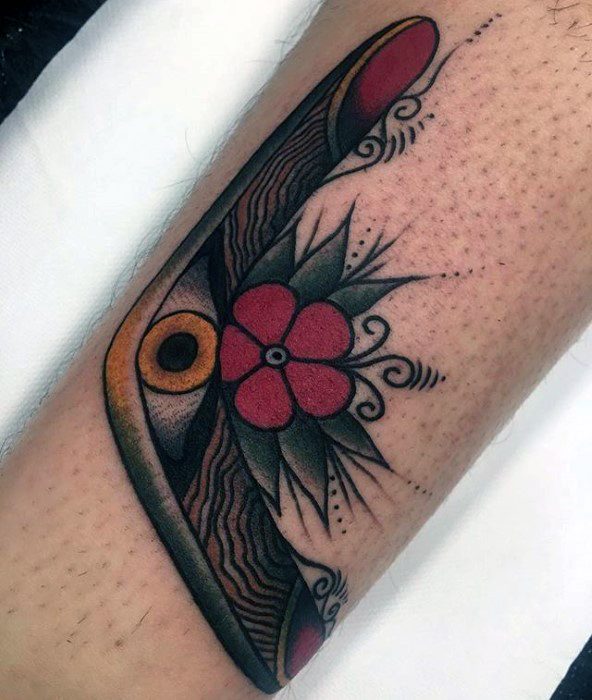 Boomerang tattoo with woodgrain detailing, a central red flower, and bold decorative elements on the forearm.