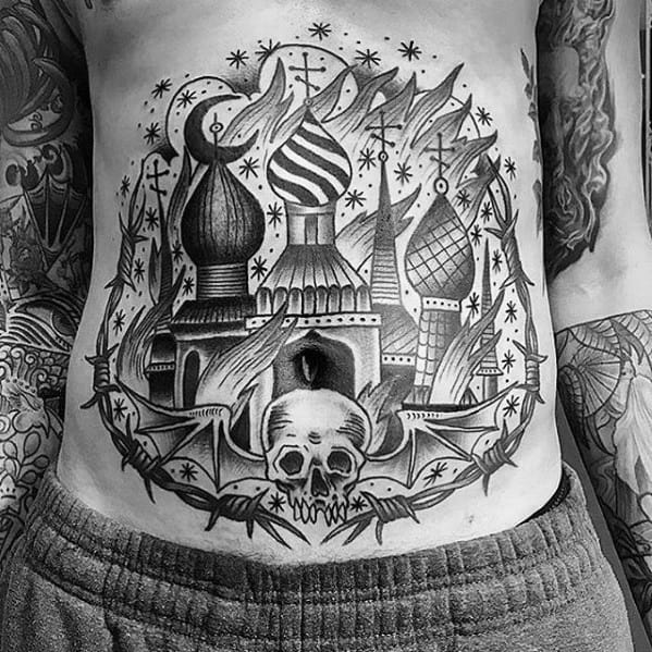 Black and grey stomach tattoo of a burning cathedral with onion domes and swirling flames. Surrounded by stars, barbed wire, and a skull.