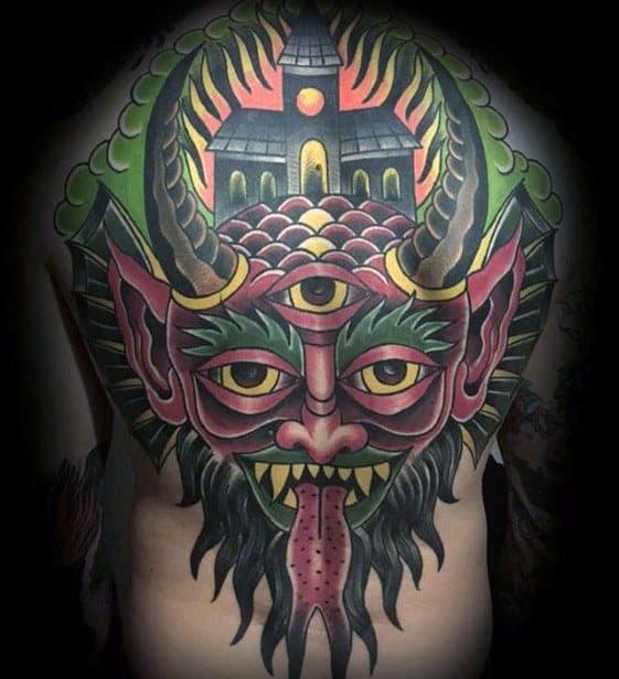 Colorful back tattoo of a horned demon with a third eye and sharp fangs. A burning church with glowing windows rises above its head.