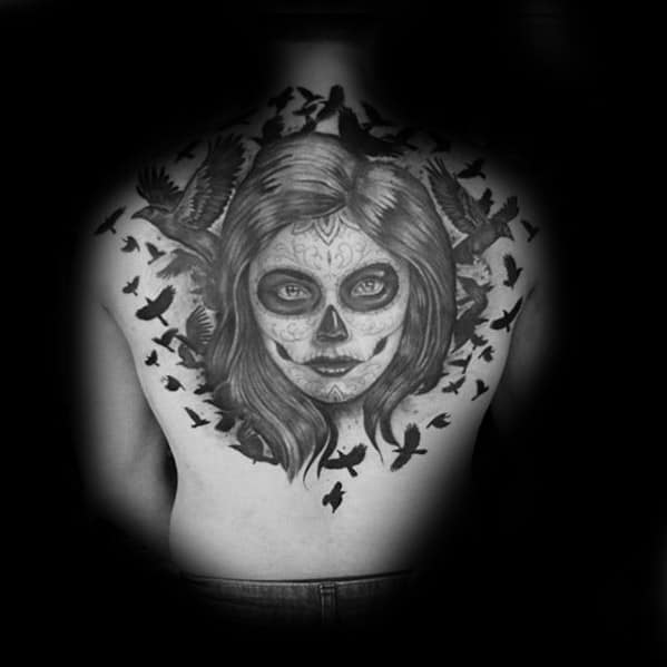 La Catrina back tattoo of a woman with sugar skull makeup, surrounded by flying black birds in a dark, atmospheric design.