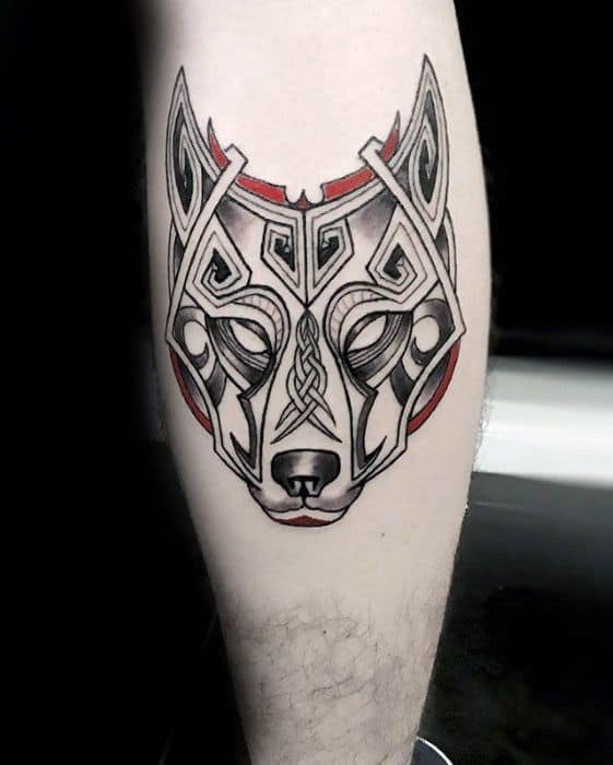 Modern Celtic wolf tattoo on calf with bold black linework, red accents, and symmetrical knot patterns forming a stylized wolf face.