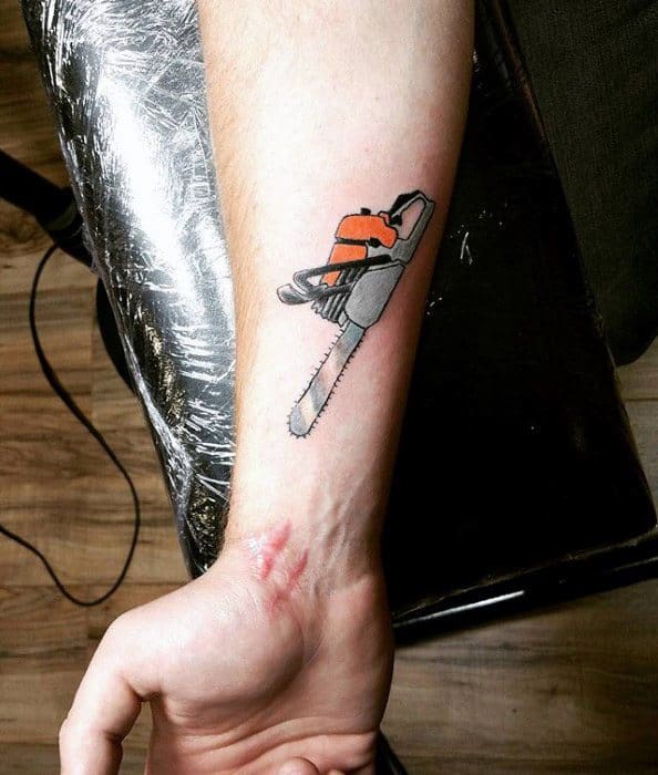 Small forearm tattoo of an orange and black chainsaw with fine detailing, placed near a visible scar for a striking contrast.