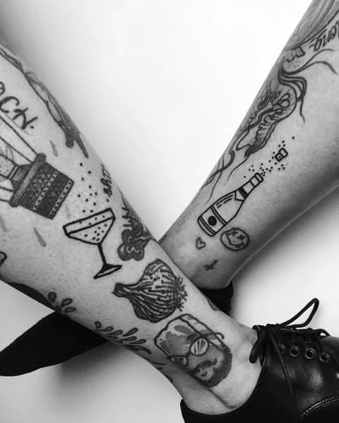 Black ink tattoos featuring a champagne bottle, glass, and bubbles, surrounded by various quirky and minimalist designs on both legs.