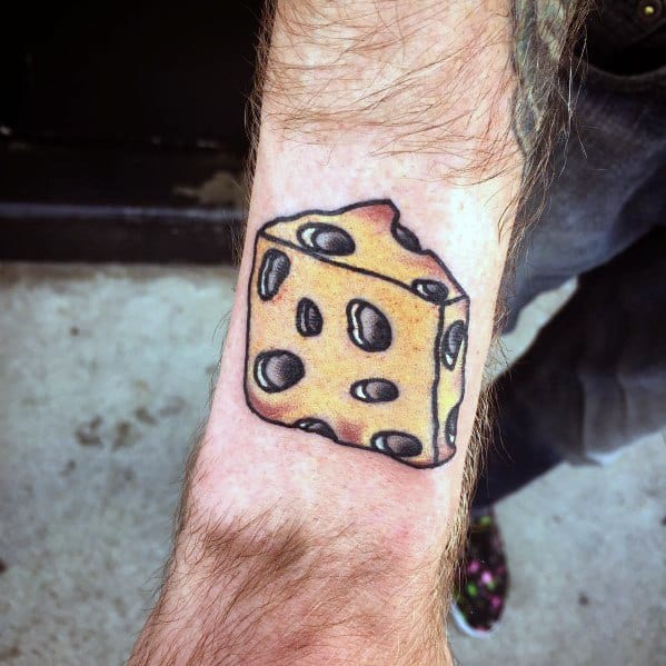 Colorful tattoo of a wedge of Swiss cheese on the wrist, featuring bold black outlines, yellow shading, and a slightly cartoonish style with exaggerated holes.