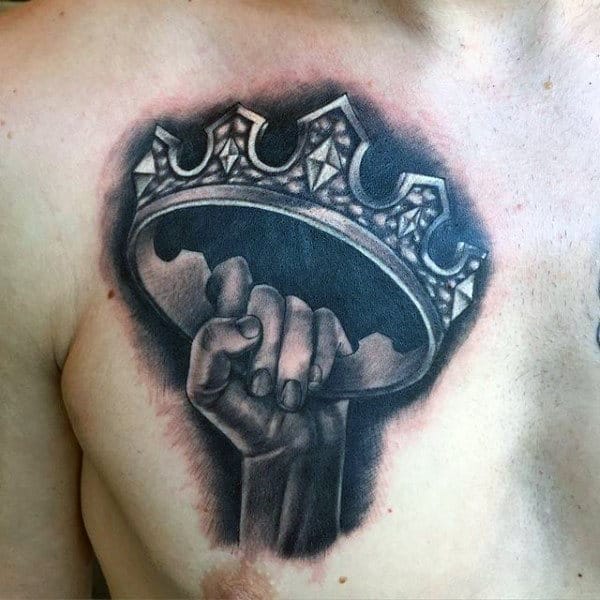 Black and grey chest tattoo of a hand holding a detailed, ornate crown