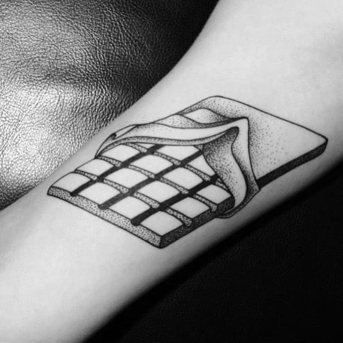 This tattoo showcases a detailed black-and-white chocolate bar with a peeled wrapper, featuring fine dot work and shading for a realistic effect.