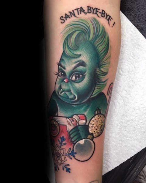 Christmas tattoo of a stylized Grinch with dramatic makeup, holding ornaments and a snowflake, with "SANTA, BYE-BYE!" text for a sassy holiday twist.