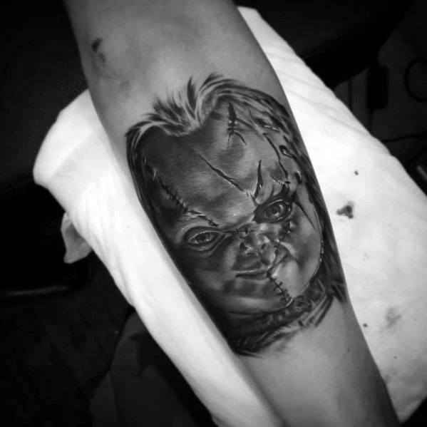 Black and grey Chucky tattoo with deep shading, featuring his stitched face, eerie grin, and intense gaze for a bold horror-inspired design.