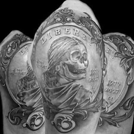 Ornate tattoo of a skeleton-themed Liberty coin, featuring intricate shading, filigree details, and a gothic-inspired design on the upper arm.